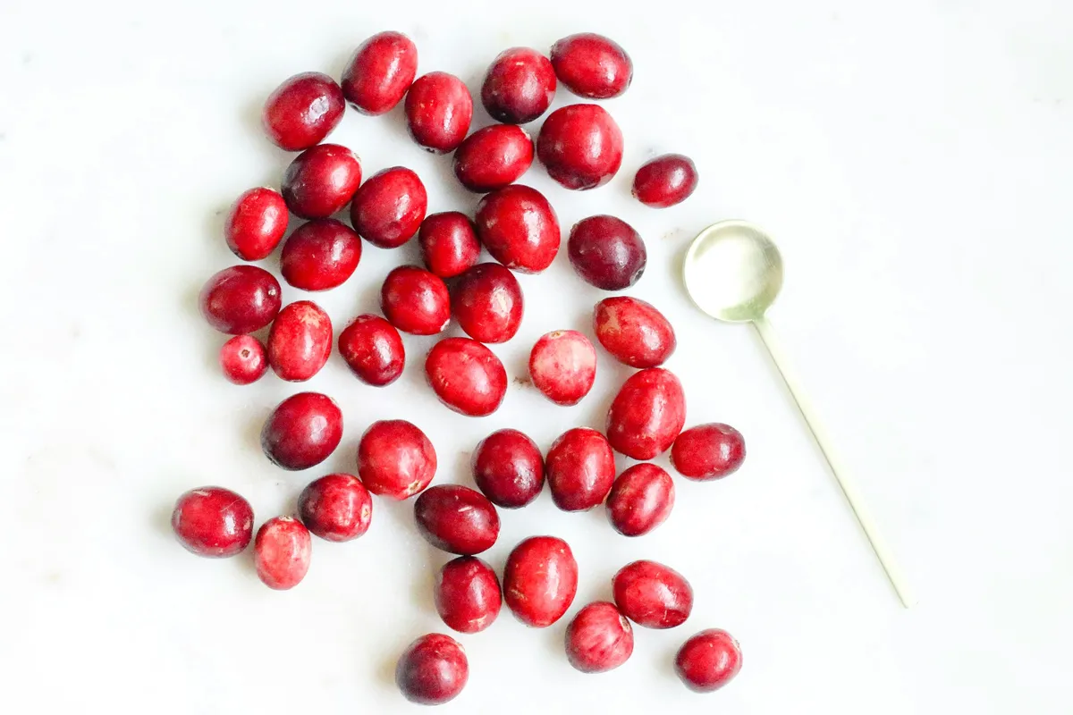 Fresh red cranberries scattered on a white marble surface next to a small spoon