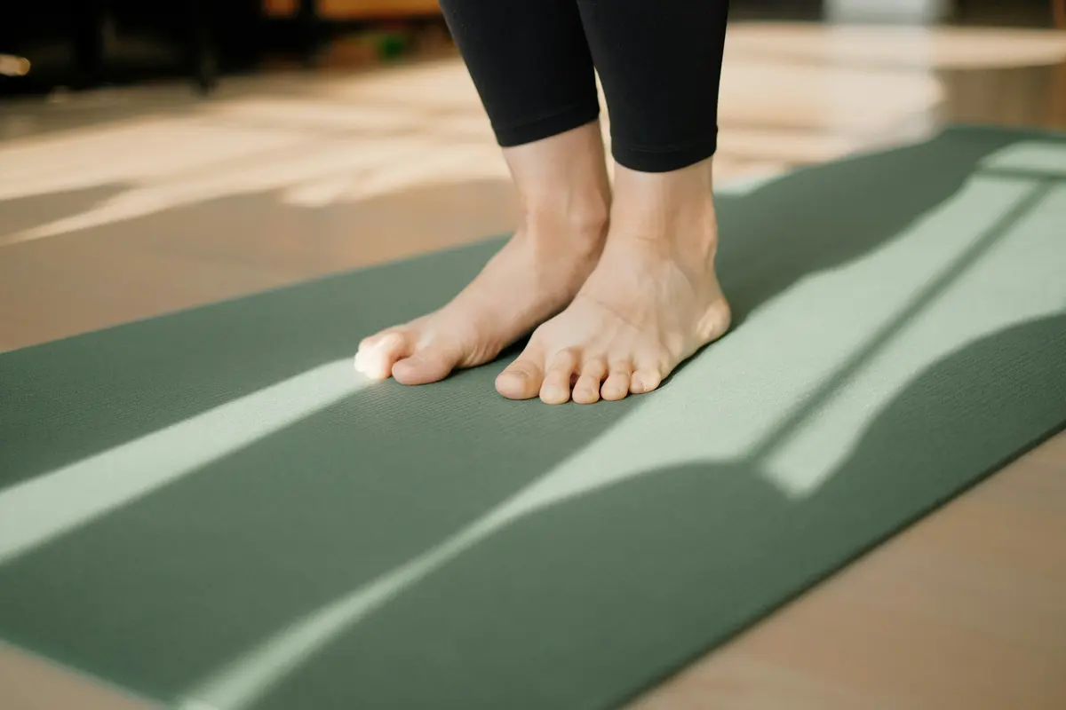 Bare feet standing on a green exercise mat in soft sunlight
