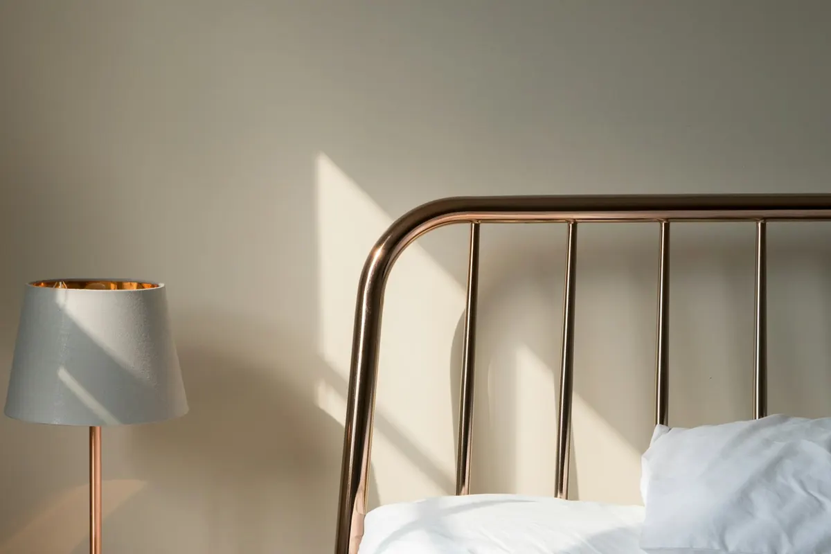 Bedside lamp and a metal bed frame with white bedding in a calm, softly lit bedroom