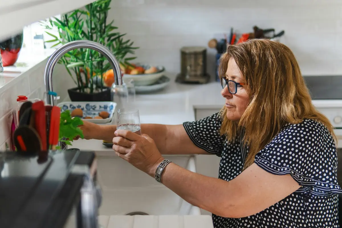 Woman in her fifties filling a glass of water at her kitchen sink